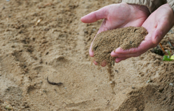 Sand rinnt aus zwei nebeneinander gehaltenen Händen.