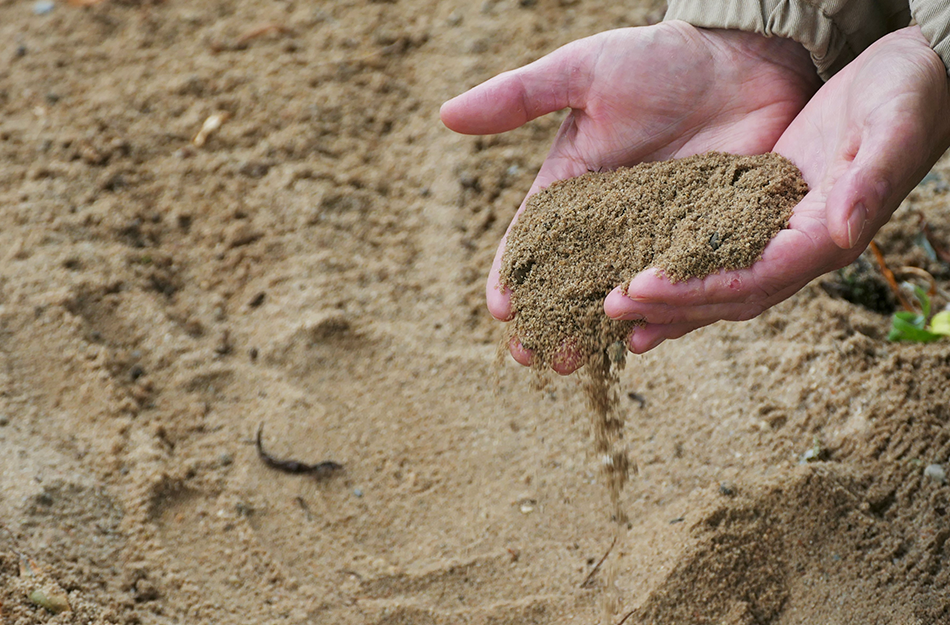 Sand rinnt aus zwei nebeneinander gehaltenen Händen.