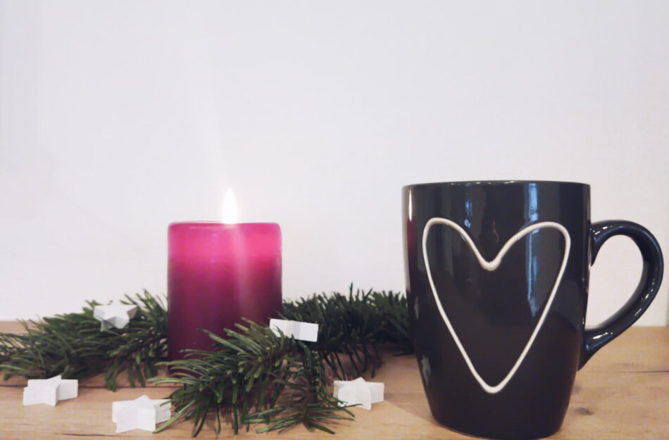 Eine Teetasse steht vor einem Weihnachtszweig mit roter Kerze.