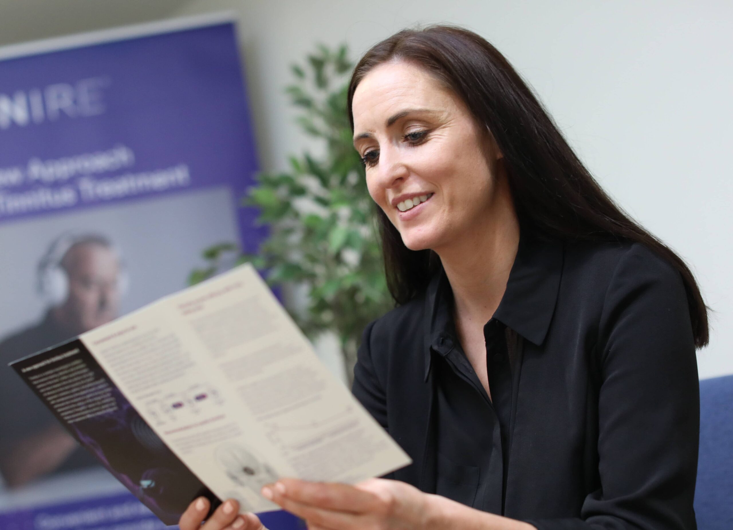 Eine Frau informiert sich in einer Broschüre zu Ursachen und Behandlung von Tinnitus.