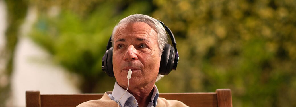 Older man sitting outside on a chair, looking into the distance. He looks relaxed and content while using the lenire device.