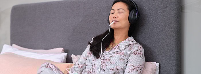 What is Lenire? Benefit 3. Woman sitting in bed with her eyes closed, looking very relaxed while using the Lenire device.