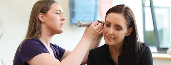 Focused Health Care Provider performing a tinnitus assessment on a relaxed patient.